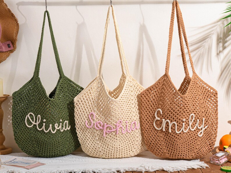 May include: Three crochet tote bags in olive green, cream, and brown, each with a name embroidered on the front: Olivia, Sophia, and Emily. The bags have long handles and a woven design, perfect for carrying items.