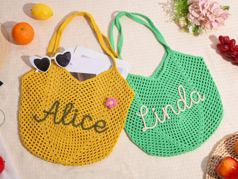 May include: Two crochet tote bags, one yellow and one green, with long handles. The yellow bag has the name "Alice" embroidered in green, and the green bag has the name "Linda" embroidered in white. Heart-shaped sunglasses rest on the yellow bag.