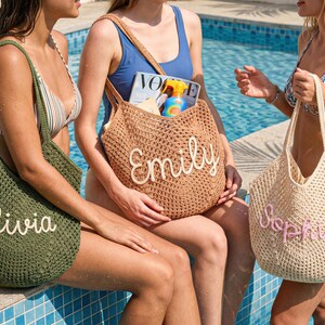 May include: Three crochet tote bags in olive green, tan, and cream, each with a name embroidered on the front: Olivia, Emily, and Sophia. The bags are open-topped and appear to be beach or pool-themed.