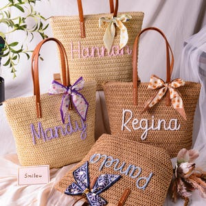 May include: Four woven straw tote bags with brown leather handles and decorative fabric ribbons. Each bag features a personalised name embroidered in cursive script: Hannah, Mandy, Regina, and Pamela. A small card with the text Smile is included.