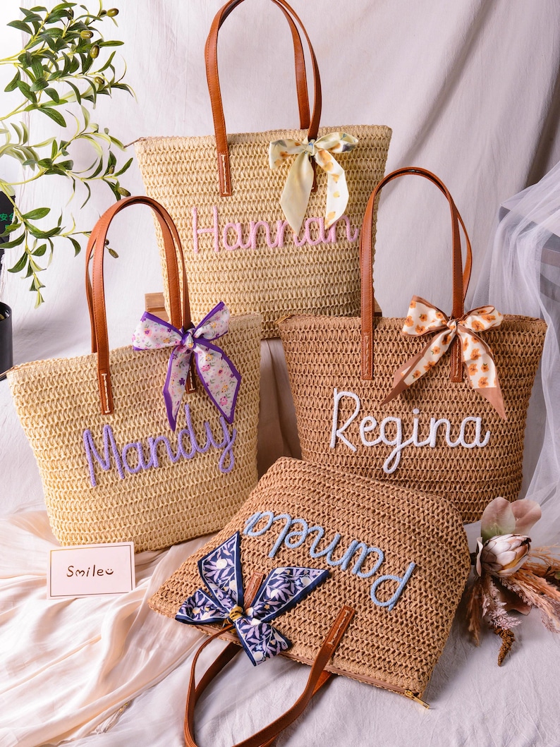 May include: Four woven straw tote bags with brown leather handles and decorative fabric ribbons. Each bag features a personalised name embroidered in cursive script: Hannah, Mandy, Regina, and Pamela. A small card with the text Smile is included.