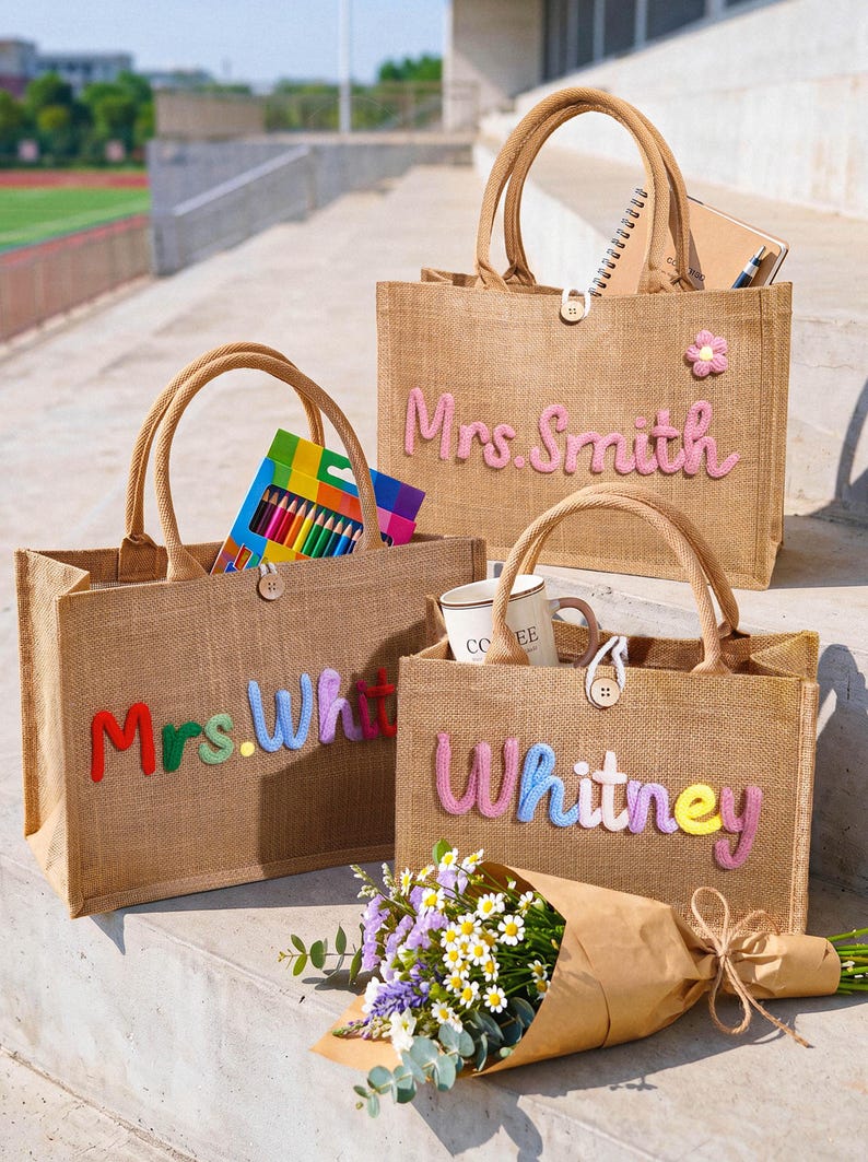 May include: Three rectangular tan jute tote bags with two top handles and a single wooden button closure. Each bag features colorful, raised, embroidered lettering on the front: one reads Mrs. Smith, one reads Mrs. Whit, and one reads Whitney.