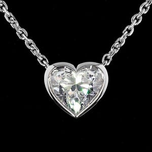 May include: A silver necklace featuring a heart-shaped diamond pendant. The clear, faceted diamond is set in a bezel. The chain is a delicate link style. The background is black.