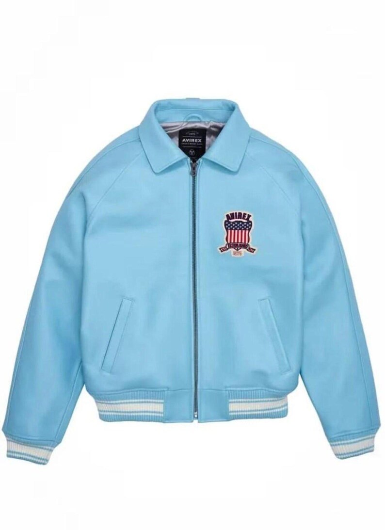 Puede incluir: Chaqueta azul claro con cremallera, cuello y dos bolsillos delanteros. La chaqueta presenta un dise&ntilde;o de rayas blancas y azul claro en los pu&ntilde;os y el dobladillo. Un parche bordado con el texto "AVIREX" est&aacute; en el pecho.