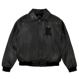 May include: Black leather jacket with a collared neckline, a zipper closure, and a black emblem on the chest. The jacket has two front pockets and ribbed cuffs and hem. The jacket is a classic style.