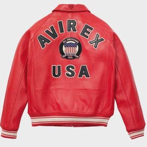 May include: A red leather jacket featuring the word "AVIREX" across the shoulders. Below is a circular patch with "ALL AMERICANS" and "ESTABLISHED 1975". The word "USA" is below the patch. The jacket has a white and red striped trim at the waist and cuffs.