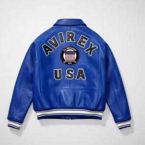 May include: A bright blue leather varsity jacket featuring the text AVIREX in large black letters across the upper back. Below the text is a circular patch with an American flag design and the text USA in large black letters at the bottom.