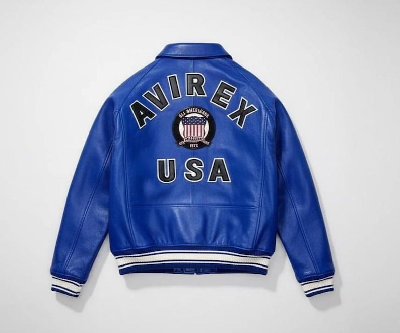 May include: A bright blue leather varsity jacket featuring the text AVIREX in large black letters across the upper back. Below the text is a circular patch with an American flag design and the text USA in large black letters at the bottom.