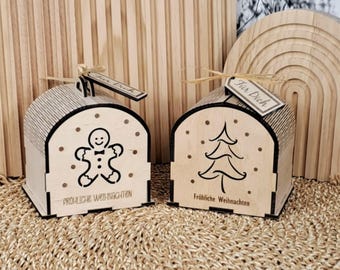 May include: Two small wooden gift boxes with arched roofs, decorated with a gingerbread man and a Christmas tree. Each box has a tag that says "Für Dich". The boxes are on a woven mat, with wooden arches in the background.