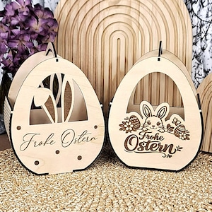 May include: Two wooden Easter egg-shaped baskets with cut-out designs and the words "Frohe Ostern." One features bunny ears, the other a bunny with eggs and flowers. The baskets are light brown with black accents.