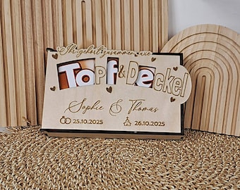 May include: A wooden wedding gift with the words "Topf & Deckel" and the names "Sophie & Thomas" engraved. The dates 25.10.2025 and 26.10.2025 are also included, along with heart and ring symbols.