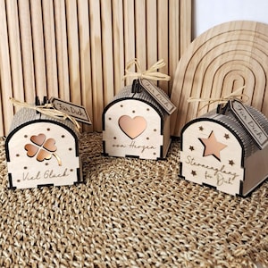 Op de afbeelding: Drie houten decoratieve dozen met uitgesneden ontwerpen. Eén heeft een klavertjevier, een andere een hart en de derde een ster. Elke doos heeft een label met de tekst "Für Dich". De dozen staan op een geweven oppervlak.