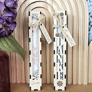 May include: Two decorative wooden candle holders with floral cutouts and attached tags. The candle holders have the words "Danke" and "Glück ist EINE MAMA WIE DICH ZU HABE" on them. One tag says "Du bist toll!!" and the other says "Nur für Dich!"