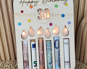 May include: Wooden birthday card with the words "Happy Birthday" and the number "30". The card has cutouts for rolled-up bills and candle-shaped lights. Colorful confetti dots are scattered around the top.