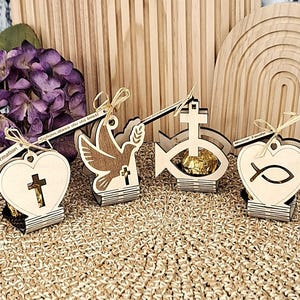 May include: Wooden religious decorations, including a heart with a cross, a dove, a fish with a cross, and a heart with a fish symbol. Each has a small tag. The background includes a wooden arch and purple flowers.