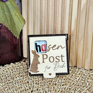 May include: A wooden box with the words "Hasen Post für Dich" and a bunny silhouette. The box has a small slot and a heart-shaped cutout. The box contains a small candy bar.