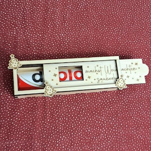 Pode incluir: Um suporte de madeira para Kinder Surpresa com um design deslizante. O suporte apresenta um design de &aacute;rvore de Natal e as palavras "macht Weihnachten zauberhaft". O ovo Kinder Surpresa &eacute; vis&iacute;vel no interior.
