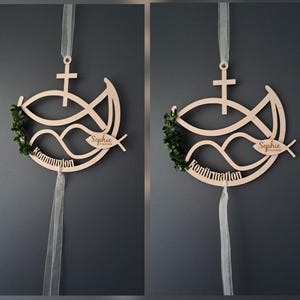 Könnte beinhalten: Hölzerne religiöse Dekoration mit Fischsymbol, Kreuz und dem Namen "Sophie" mit Datum. Das Design umfasst einen grünen Kranz und das Wort "Kommunion" oder "Konfirmation". Ein weißes Band ist zum Aufhängen befestigt.