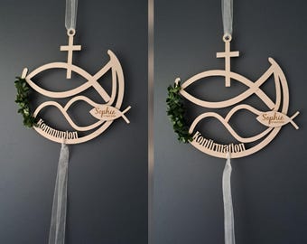 May include: Wooden religious decoration featuring a fish symbol, cross, and the name "Sophie" with a date. The design includes a green wreath and the word "Kommunion" or "Konfirmation". A white ribbon is attached for hanging.