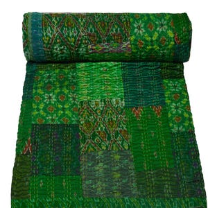May include: A green patchwork quilt with a variety of patterns and textures. The quilt is rolled up at the top, displaying a detailed design. The quilt is made of multiple fabric squares stitched together with white thread.