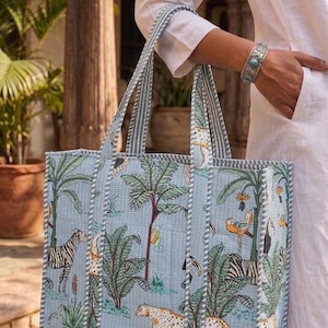K&ouml;nnte beinhalten: Hellblaue Tragetasche mit Dschungel-Motiv, das Zebras, Leoparden und Palmen zeigt. Die Tasche hat gestreifte Griffe und ein gestepptes Design. Die Tasche wird von einer Person getragen, die ein wei&szlig;es Hemd und ein silbernes Armband tr&auml;gt.