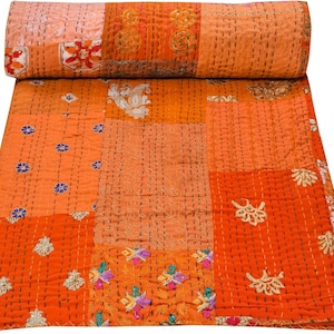 May include: An orange patchwork quilt with a rolled-up section at the top. The quilt features various shades of orange and peach, with embroidered floral and geometric patterns in gold, blue, and other colors. The quilt is made of multiple fabric squares.