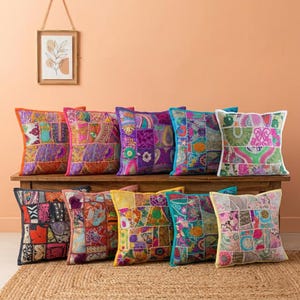 May include: A collection of square decorative throw pillows with patchwork designs in various colors, including purple, orange, pink, and teal. The pillows are arranged on a wooden bench, creating a vibrant and eclectic display.