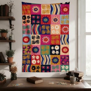 May include: A colorful tapestry with a patchwork design. The tapestry features a grid of squares, each with a unique floral or abstract pattern in vibrant colors like pink, blue, yellow, and green. The tapestry is hanging on a wall.