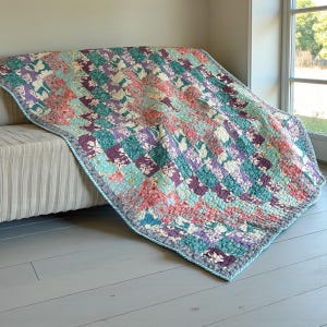 Puede incluir: Un edredón de retazos colorido con un estampado floral en tonos turquesa, morado, rosa y blanco. El edredón está drapeado sobre un sofá beige y tiene un borde azul claro. El edredón está hecho de cuadrados cosidos.