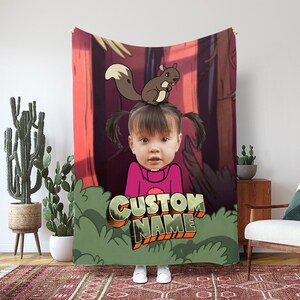 Könnte beinhalten: Eine personalisierte Decke mit einer Cartoon-Illustration eines Kindes und eines Eichhörnchens vor einem Waldhintergrund. Die Decke zeigt den Text "CUSTOM NAME" in einer stilisierten Schriftart. Das Kind trägt ein rosa Hemd.