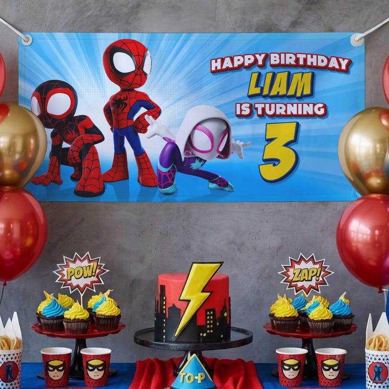Op de afbeelding: Een verjaardagsfeestje met een banner met Spider-Man-personages. De banner leest "Happy Birthday Liam is turning 3." Een taart met een bliksemontwerp en cupcakes worden tentoongesteld. Rode en gouden ballonnen maken de feestelijke decoratie compleet.
