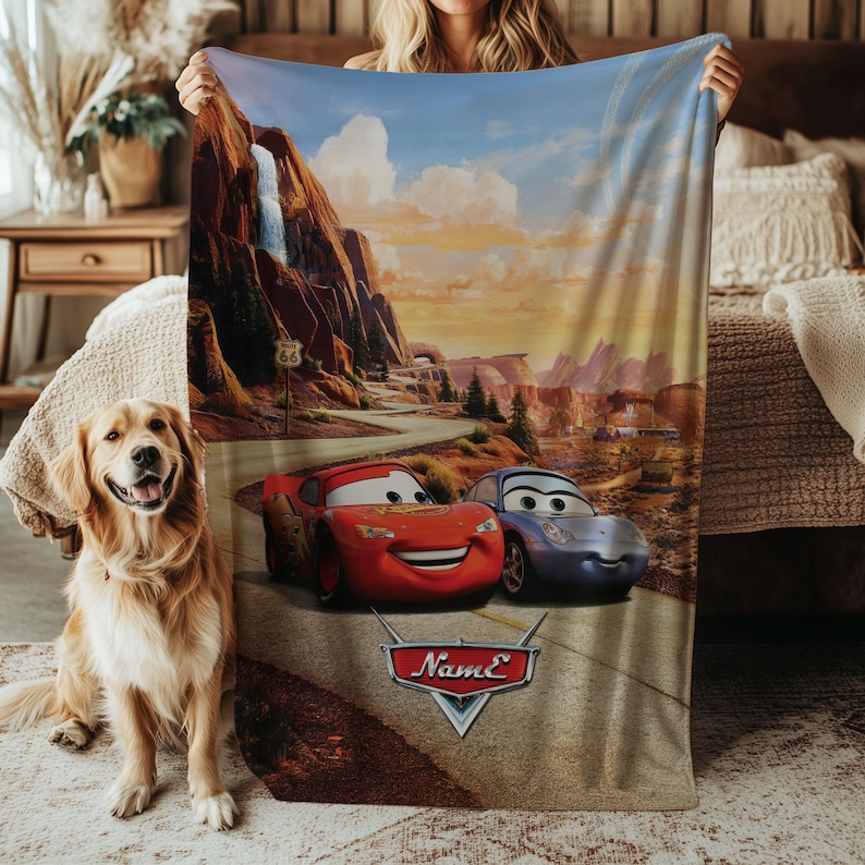 May include: A plush blanket featuring a scenic desert landscape with a waterfall and Route 66 sign. The blanket showcases the animated characters Lightning McQueen and Sally Carrera from the movie Cars. The blanket has the name "Name" on it.