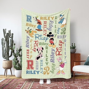 Puede incluir: Una manta verde claro con personajes de Disney: Goofy, Pluto, Mickey Mouse, Minnie Mouse, Donald Duck y Daisy Duck. La manta tiene el nombre "Riley" en varios colores y fuentes, con un fondo de patrón de cuadrícula.