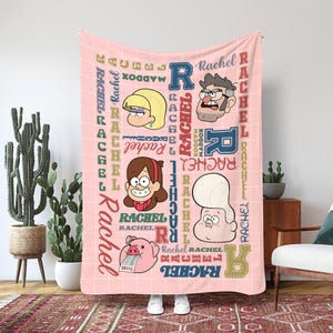 Könnte beinhalten: Eine rosa Decke mit Illustrationen von Zeichentrickfiguren und dem Namen "Rachel" in verschiedenen Schriftarten und Farben. Die Decke hat ein Gittermuster und enthält Bilder von Charakteren und den Namen "Maddox".