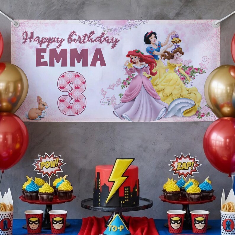 May include: A birthday party scene with a banner reading "Happy birthday EMMA 3" featuring Disney princesses. A red and black cake with a lightning bolt sits on a stand, surrounded by cupcakes, balloons, and superhero-themed cups.