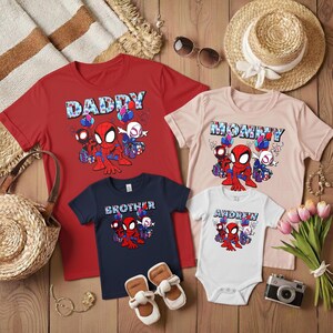 Puede incluir: Una colecci&oacute;n de camisetas rojas, rosas, azul marino y blancas y un body con gr&aacute;ficos de Spider-Man. Las camisetas tienen las palabras "Daddy", "Mommy" y "Brother" impresas. El body tiene el nombre "Andrew" impreso.