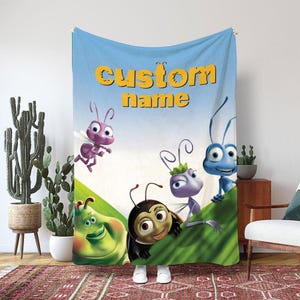 May include: A blue blanket featuring cartoon insects with the text "custom name" in yellow. The blanket has a light blue sky background and green grass. The cartoon insects are in various colors.