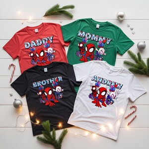 Puede incluir: Cuatro camisetas rojas, verdes, negras y blancas, cada una con un dise&ntilde;o de Spider-Man. La camiseta roja dice "DADDY", la verde dice "MOMMY", la negra dice "BROTHER" y la blanca dice "ANDREW".