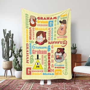 Könnte beinhalten: Eine gelbe Decke mit Cartoon-Charakteren und dem Wort "GRAHAM" in verschiedenen Farben und Schriftarten. Die Decke hat ein Gittermuster und zeigt Bilder von Charakteren mit unterschiedlichen Ausdrücken. Die Decke besteht aus einem weichen Material.