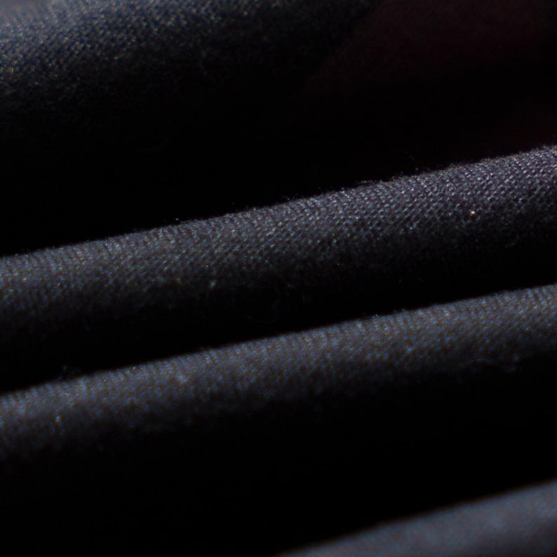 May include: Close-up of black fabric with visible texture and folds. The image highlights the material's dark color and subtle variations in the weave, suggesting a garment or textile.