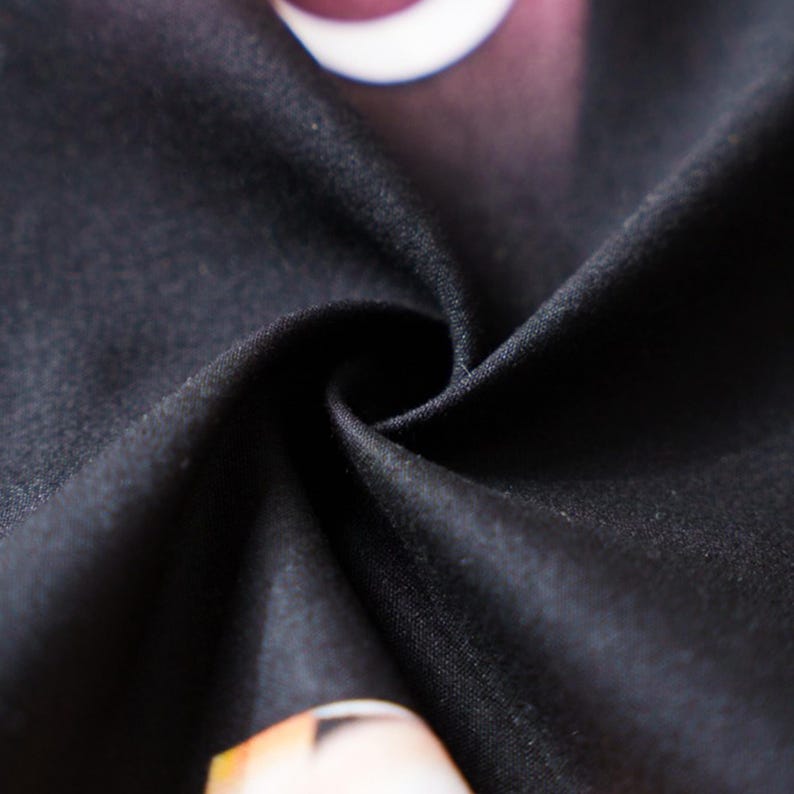 May include: Close-up of black fabric with a subtle texture, showing a swirl pattern. The fabric appears to be soft and drapes naturally. Hints of other colors are visible in the background, suggesting a printed design.