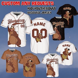 May include: Baseball jerseys in various colors, featuring a cartoon bear character. The jerseys are available in white, black, brown, and tan, with pinstripes and solid designs. Text includes "Humphrey", "Name", and "00". The jerseys are for kids, youth, and adults.