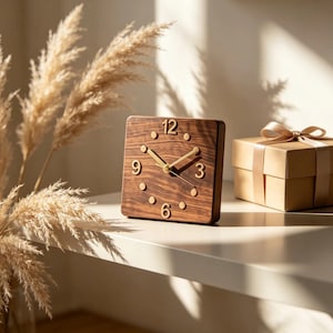 May include: A square wooden clock with a dark brown wood grain finish, featuring gold-colored hands and gold-colored numerals at the 12, 3, 6, and 9 positions, with small gold dots marking the remaining hours on the clock face.