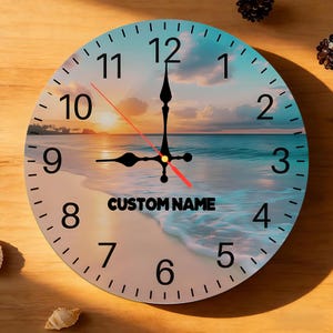 May include: A round wall clock featuring a sunset beach scene with ocean waves, black numerals, and black ornate hands with a red second hand. The text CUSTOM NAME is printed in black in the centre of the clock face over the water and sand.