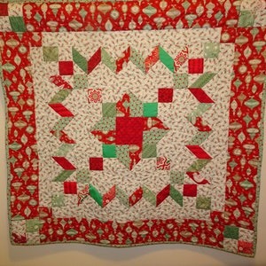 May include: A red and green patchwork quilt with a starburst design in the center. The quilt is edged with a red and green border with a pattern of Christmas ornaments.