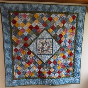 May include: A square patchwork quilt featuring a central panel with a butterfly and floral print surrounded by a diamond-shaped light blue border. The quilt is composed of small multi-colored fabric squares in red, yellow, and blue tones.