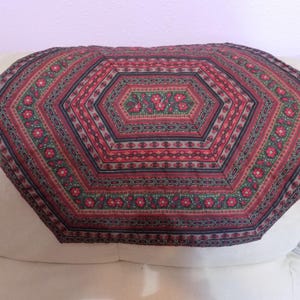 May include: A hexagonal fabric mat featuring a repeating pattern of red flowers on a dark green background, bordered by concentric bands of deep red, black, and intricate geometric motifs in shades of maroon, black, and muted green throughout.