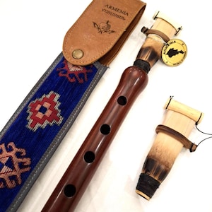 Pode incluir: Um duduk castanho escuro, um instrumento de sopro de palheta dupla, com um estojo de couro e uma palheta sobressalente. O estojo é de couro castanho com a palavra "Armenia" e um desenho de romã. O duduk tem quatro orifícios para os dedos.