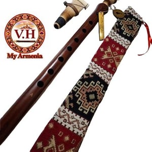 Puede incluir: Una flauta duduk de madera marrón oscuro con una boquilla de caña separada, acompañada de un estuche de tela largo y estrecho con un patrón geométrico en colores rojo, negro y crema. Una pequeña etiqueta rectangular está unida al instrumento.