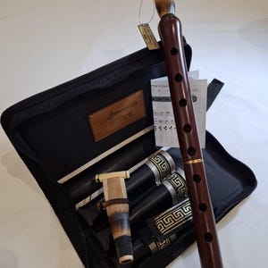 Könnte beinhalten: Ein dunkelbraunes armenisches Duduk-Blasinstrument mit einem Rohrblatt und einem schwarzen Etui. Das Etui ist geöffnet und zeigt das Instrument und seine Teile. Der Text "Armenian Duduk" ist auf dem Etui zu sehen.